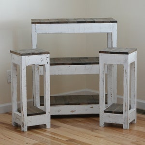 May include: Three white wooden tables with distressed paint. The largest table has two shelves and the two smaller tables have one shelf each.