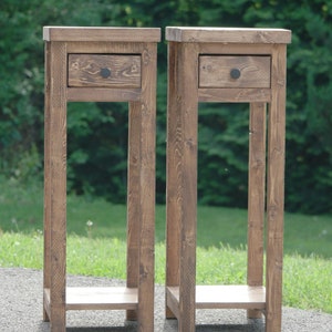 May include: Two wooden end tables with a single drawer and a lower shelf. The tables are stained a dark brown color and have black metal drawer pulls.