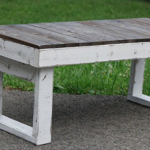 May include: A whitewashed wooden coffee table with a distressed finish. The top is made of dark stained wood planks.