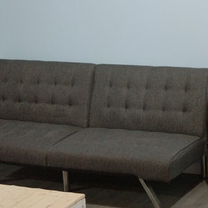 May include: A grey futon sofa with a tufted back and two wooden end tables with a light wood top and dark brown legs.