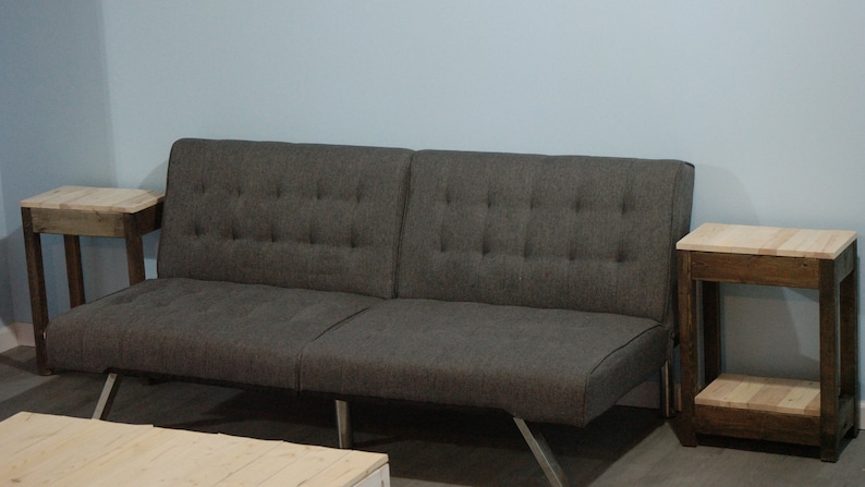 May include: A grey futon sofa with a tufted back and two wooden end tables with a light wood top and dark brown legs.