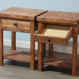 May include: Two matching brown wooden nightstands, each featuring a square top, a single drawer with a small black circular knob, and an open lower shelf. One nightstand has its drawer closed, while the other has its drawer pulled open.
