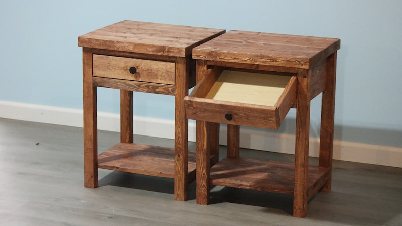May include: Two matching brown wooden nightstands, each featuring a square top, a single drawer with a small black circular knob, and an open lower shelf. One nightstand has its drawer closed, while the other has its drawer pulled open.