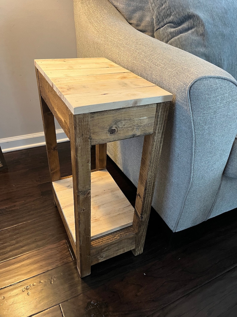 May include: A rustic wooden end table with a light wood top and a lower shelf. The table is stained a dark brown colour and has a simple, farmhouse style.