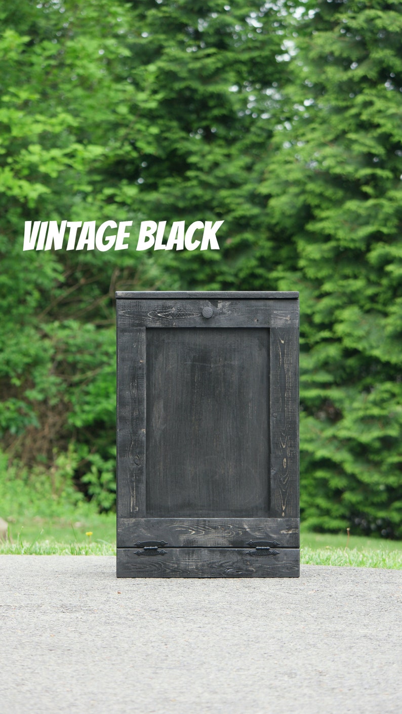 May include: A black wooden trash can with a single door and two metal handles. The can is sitting on a gray asphalt surface. The text "Vintage Black" is visible in the image.