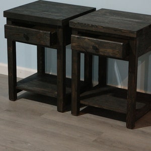 May include: A pair of dark brown wooden nightstands, each featuring a square top, a single pull-out drawer with a small round knob, four straight legs, and an open lower shelf. The wood grain is visible throughout the dark stained finish.