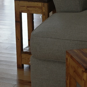 May include: A gray fabric sofa with a wooden end table next to it. The end table has a simple design with a shelf and is made of unfinished wood.