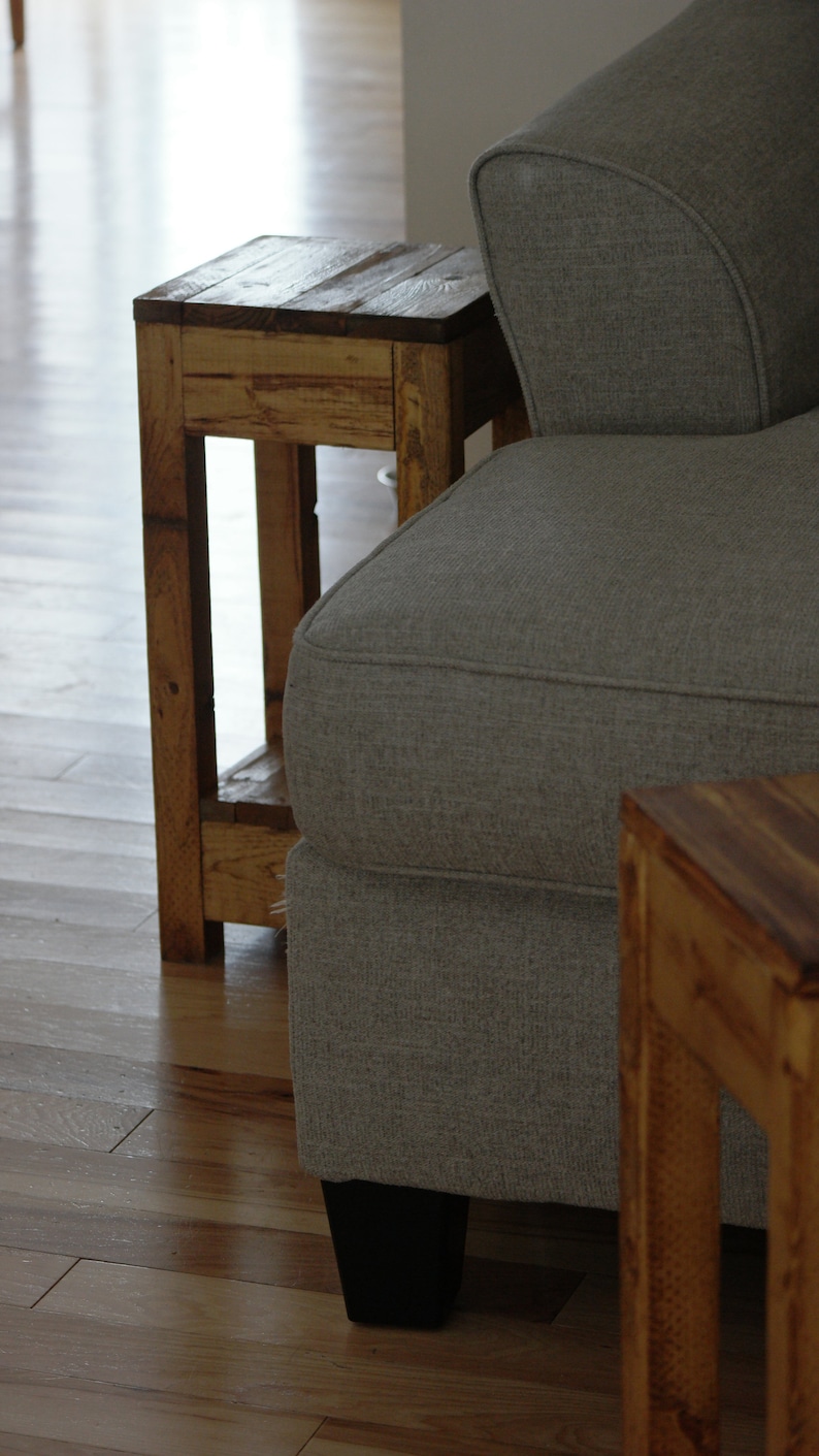 May include: A gray fabric sofa with a wooden end table next to it. The end table has a simple design with a shelf and is made of unfinished wood.