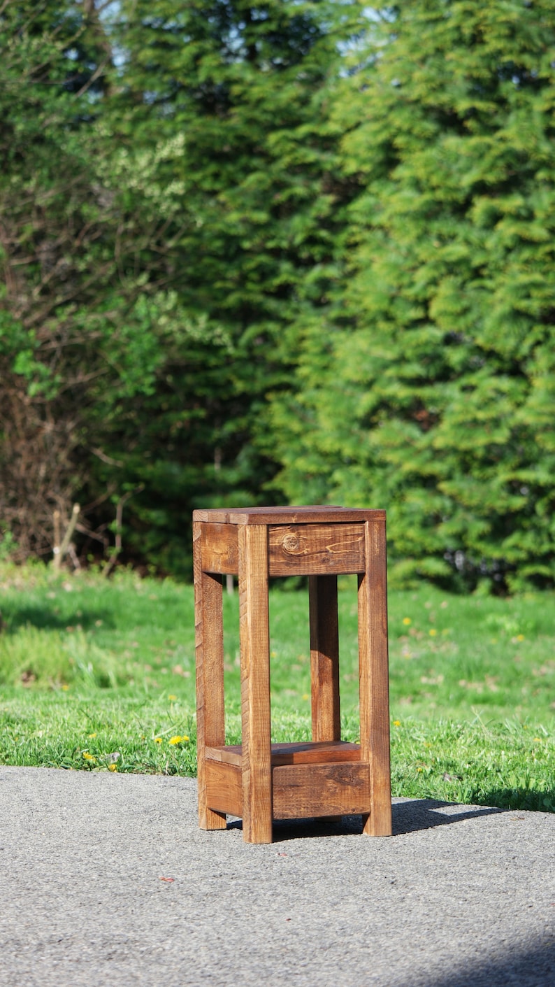 May include: A rustic wooden side table with a dark brown stain. The table has a simple design with a square top and four legs.