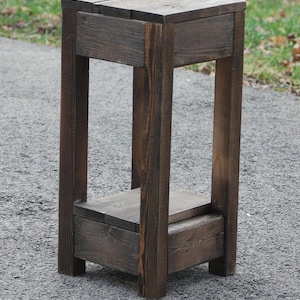 May include: A dark brown wooden plant stand with two shelves. The stand is made of reclaimed wood and has a rustic look.