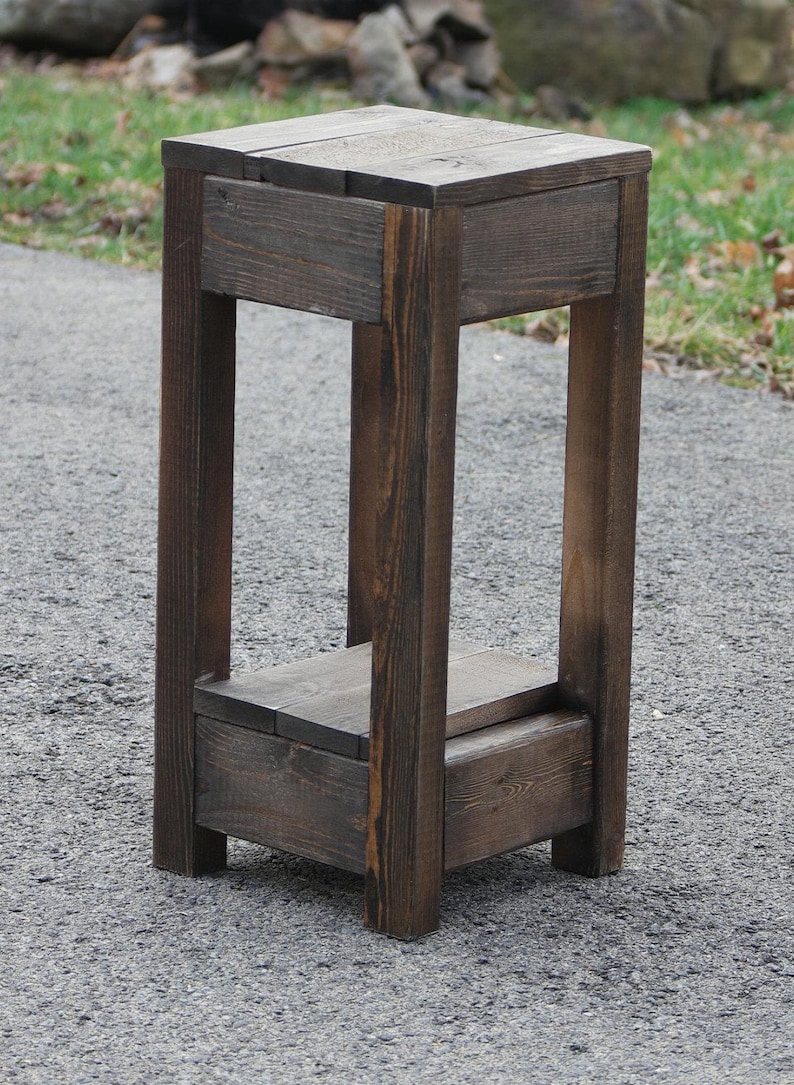 May include: A dark brown wooden plant stand with two shelves. The stand is made of reclaimed wood and has a rustic look.