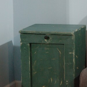 May include: A green wooden trash can with a hinged door and a black knob. The can has a distressed finish and black metal hinges.