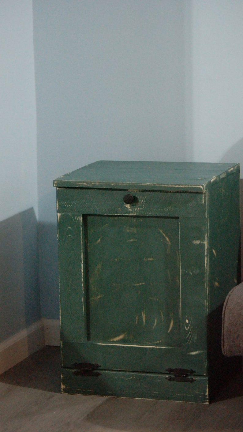May include: A green wooden trash can with a hinged door and a black knob. The can has a distressed finish and black metal hinges.