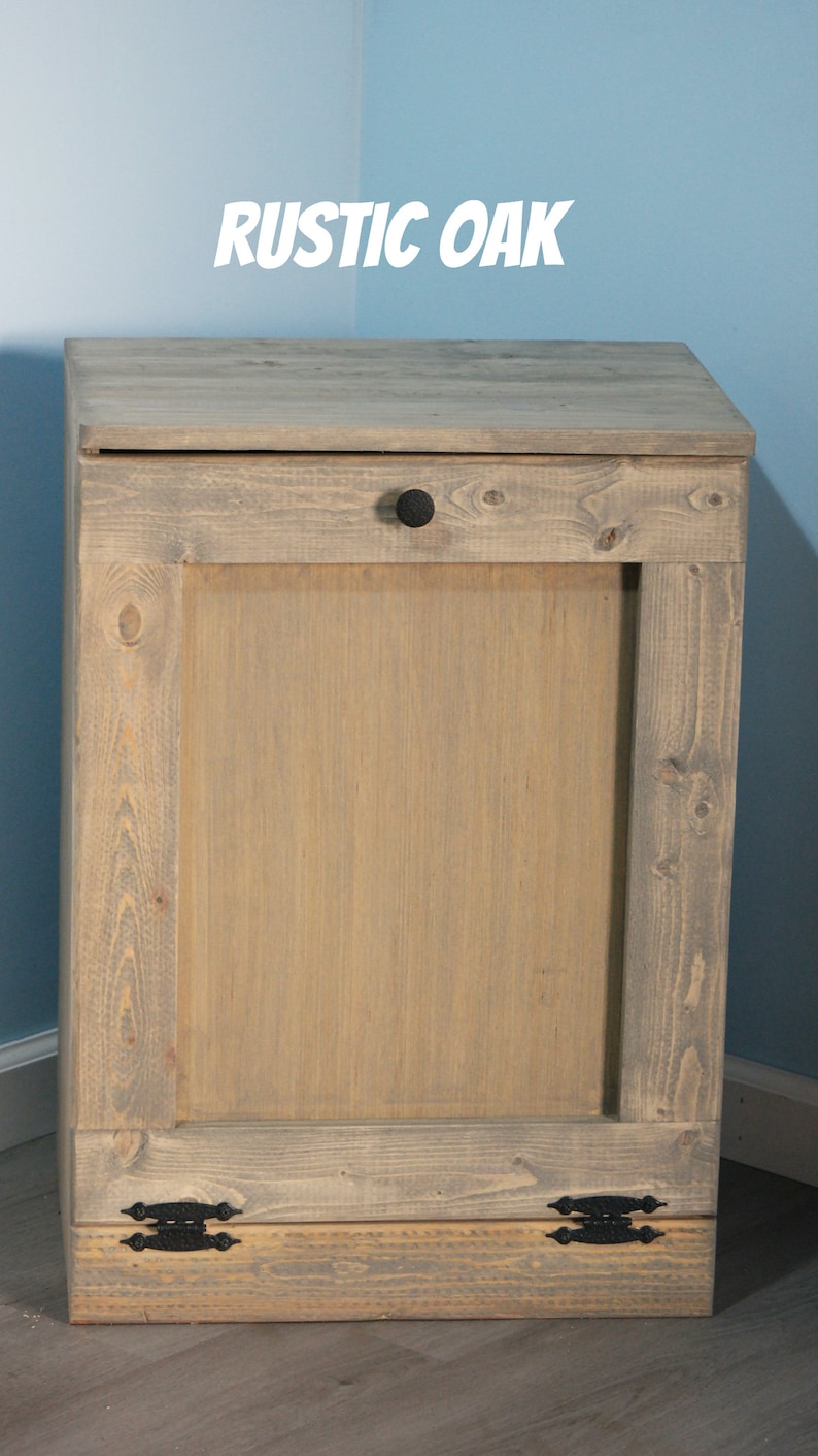 May include: A rustic oak trash can with a single door and black hardware. The can has a distressed wood finish and is made of solid wood.