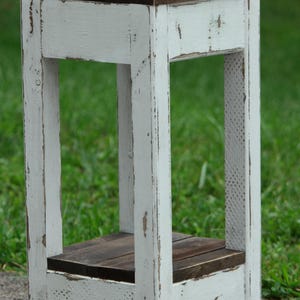 May include: White wooden end table with a distressed finish and a dark brown top. The table has a shelf and is perfect for a small space.