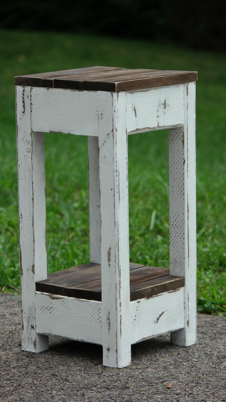 May include: White wooden end table with a distressed finish and a dark brown top. The table has a shelf and is perfect for a small space.