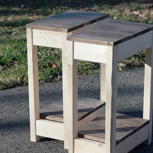 May include: Two wooden end tables with a light brown stain. The tables have a single shelf and a square top.