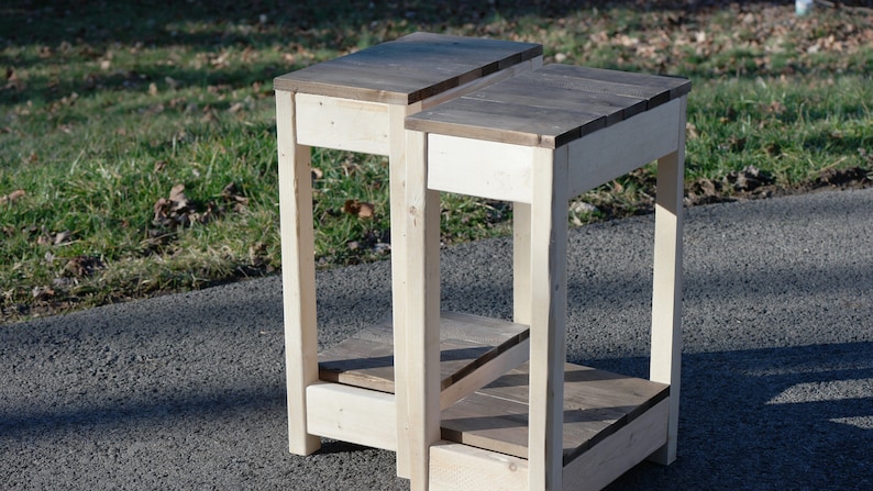 May include: Two wooden end tables with a light brown stain. The tables have a single shelf and a square top.