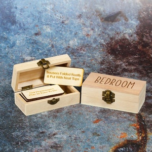 Wooden storage box with Bedroom written on the lid of it. Next to it is an open box with engraved tokens such as Trousers folded neatly and put with neat tops on.