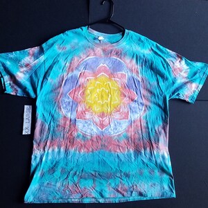 May include: A tie-dye t-shirt with a colorful mandala design in the center. The shirt is a teal blue color with pink, yellow, and purple accents. The shirt is labeled "XX Large".