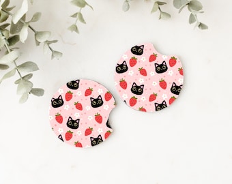 May include: Two pink and white round coasters with a black cat and red strawberry pattern.