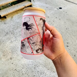 May include: A frosted glass water bottle with a black and white anime graphic print. The graphic features multiple characters from the anime series Inuyasha. The bottle has a red and white lid.