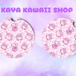 May include: Two round car coasters with a pink pattern featuring cartoon characters and stars. The coasters have a small notch on one side. The text "KAYA KAWAII SHOP" is above the coasters in a purple font.