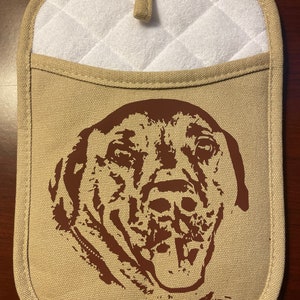 May include: A tan canvas pot holder with a white quilted pocket and a brown silhouette of a dog's face.