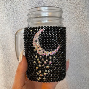 May include: A clear glass mason jar with a black rhinestone cover featuring a crescent moon and stars design.