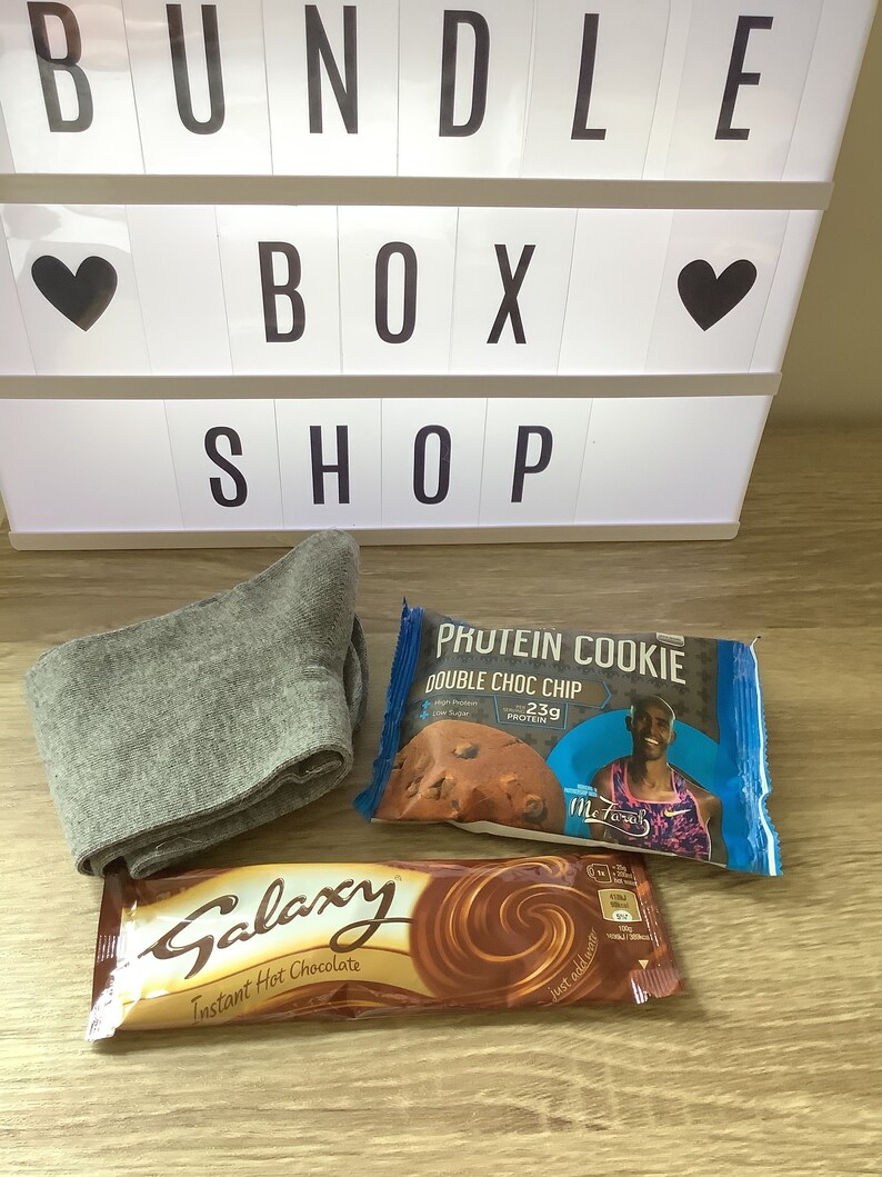 May include: A gray pair of socks, a brown chocolate bar with the text "Galaxy Instant Hot Chocolate", and a blue protein cookie package with the text "Phutein Cookie Double Choc Chip 23g Protein" and a picture of a person running.
