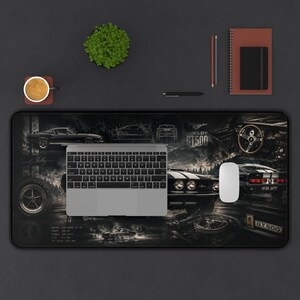 May include: A rectangular desk mat featuring a black and white graphic print of a 1967 Shelby GT500 car, including multiple views of the vehicle, the text Shelby GT500, and technical specifications. A silver laptop and a white computer mouse sit on top.