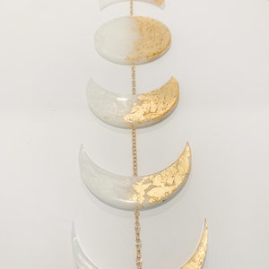 May include: A gold and white moon phase wall hanging with a chain connecting each crescent moon shape.