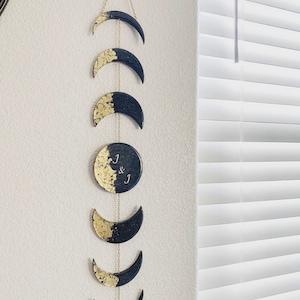 May include: A black and gold moon phase wall hanging with the initials "J & J" on the full moon.
