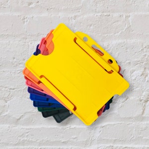 May include: A stack of colourful plastic ID card holders. The top holder is yellow and has a slot for a card. The other holders are orange, red, blue and green.
