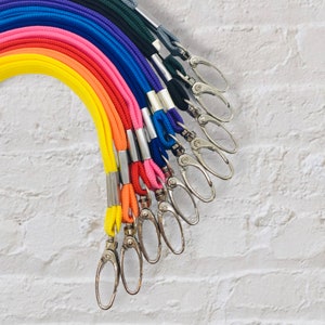 May include: A rainbow assortment of colourful lanyards with silver swivel clasps. The lanyards are made of a woven cord material.