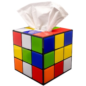 May include: A colorful tissue box cover shaped like a Rubik's Cube. The box is made of plastic and has a black base with nine squares on each side. The squares are in different colors, including red, yellow, green, blue, orange, and white.