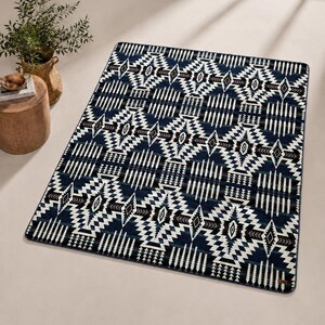 May include: A rectangular rug with a geometric pattern in navy blue, white, and brown. The design features diamond and zigzag shapes. The rug is placed on a light-colored surface.