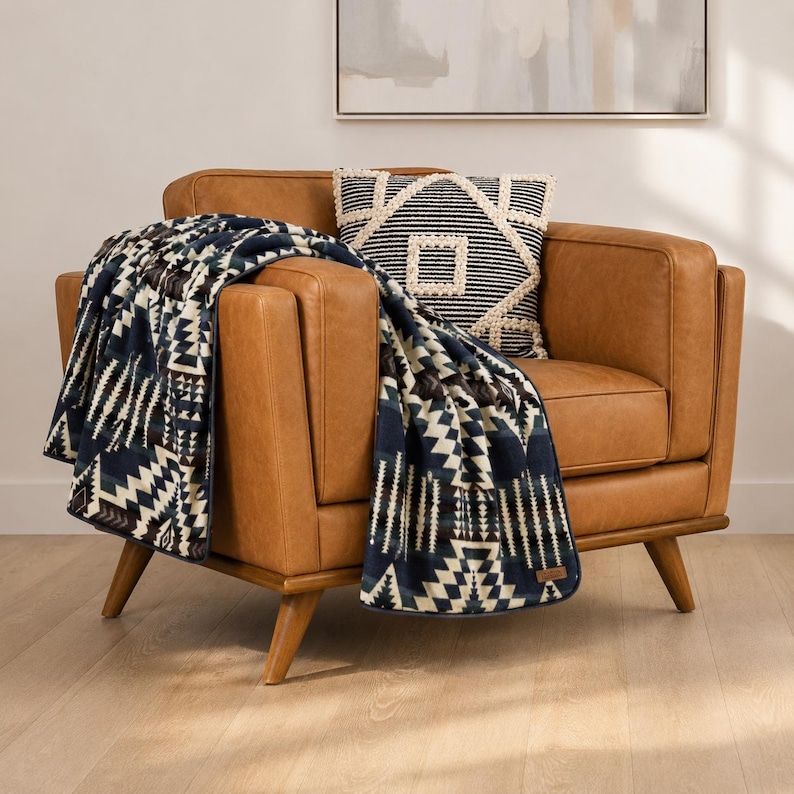 May include: A brown leather armchair with a patterned throw blanket and decorative pillow. The blanket features a geometric design in navy blue, white, and brown. A matching pillow with a geometric pattern sits on the chair.