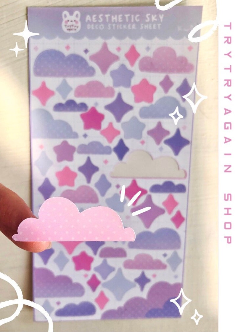 May include: A sheet of pastel purple, pink, and white aesthetic sky stickers featuring clouds and stars. The sticker sheet says "Aesthetic Sky Deco Sticker Sheet" at the top.