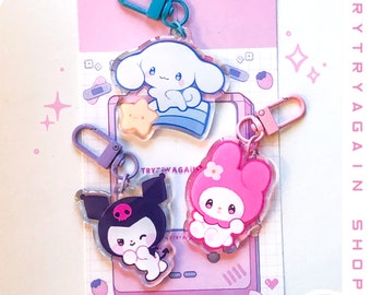 May include: Three colorful character charms with keychains. The charms are made of clear acrylic and feature a pink bunny, a black and white cat, and a white dog. The charms are on a pink background with white text that says "TRY TRY AGAIN SHOP".