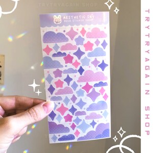 May include: A sheet of pastel purple, pink, and blue aesthetic sky themed stickers featuring clouds and stars. The sticker sheet is labeled "Aesthetic Sky Deco Sticker Sheet".