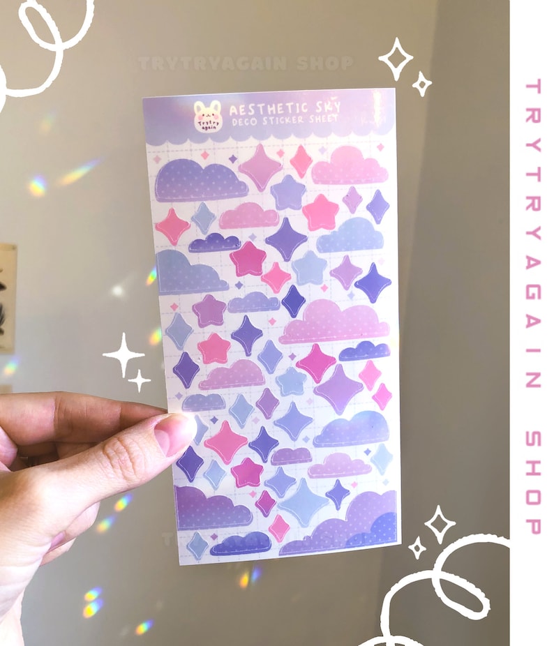 May include: A sheet of pastel purple, pink, and blue aesthetic sky themed stickers featuring clouds and stars. The sticker sheet is labeled "Aesthetic Sky Deco Sticker Sheet".