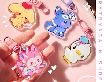 May include: Four colorful keychains featuring cartoon characters. The keychains are made of clear plastic with a printed design. The characters include a yellow dog, a blue and white cat, a pink and white cat, and a white duck.