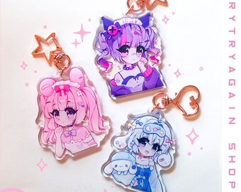 May include: Three anime-style character charms with gold keychains. The charms are made of clear acrylic and feature a pink-haired girl with pigtails, a purple-haired girl with cat ears, and a white-haired girl with a blue and white outfit.