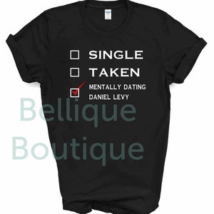 May include: Black t-shirt with white text that reads "Single, Taken, Mentally Dating Daniel Levy" with a checkmark next to the last option.