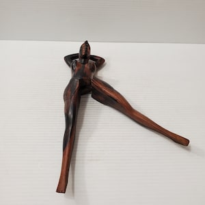 Puede incluir: Un cascanueces de madera con forma de mujer, con un acabado de madera de grano marrón oscuro y negro. La mujer está reclinada con los brazos detrás de la cabeza.