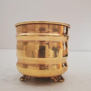May include: A gold-coloured brass planter with a fluted design and three decorative feet.