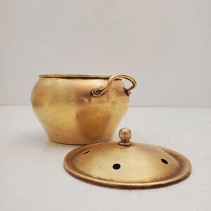 May include: A gold brass incense burner with a lid and a handle. The lid has small holes for the incense to burn through.