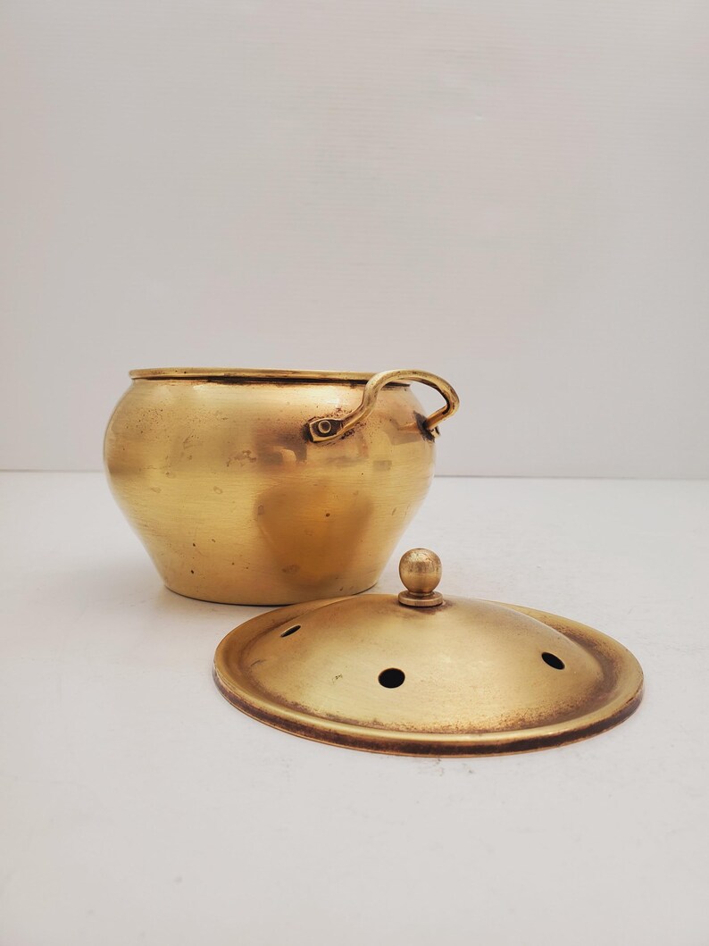 May include: A gold brass incense burner with a lid and a handle. The lid has small holes for the incense to burn through.