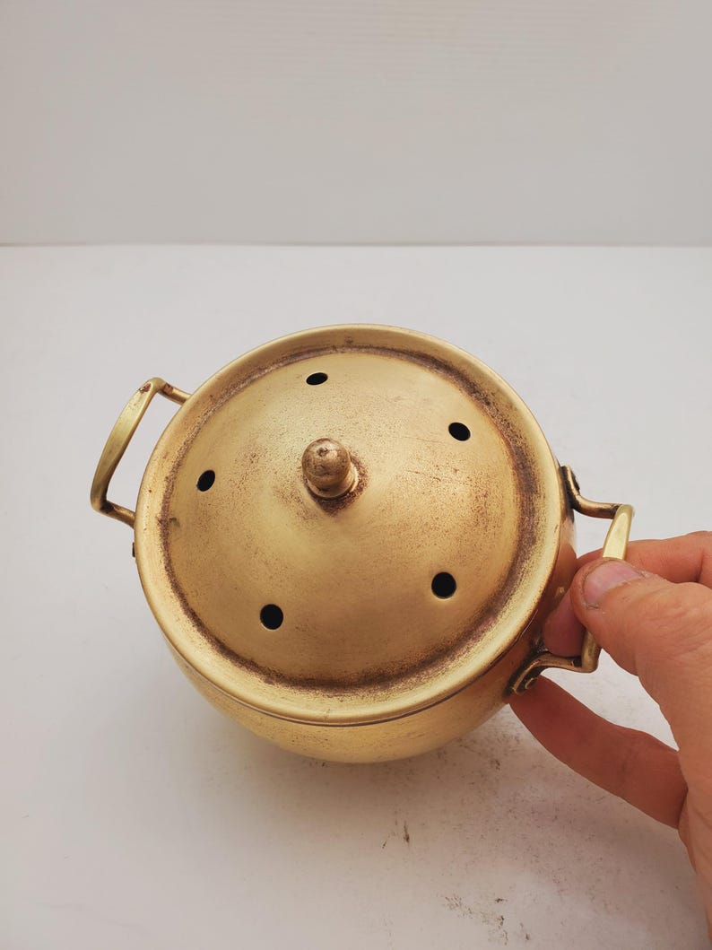 May include: A gold metal incense burner with a lid and two handles. The lid has several small holes for the incense to burn through.